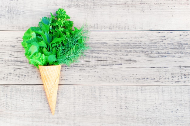 Ice cream cone with fresh herbs on a wooden. Lettuce, parsley, dill, garlic flower. 