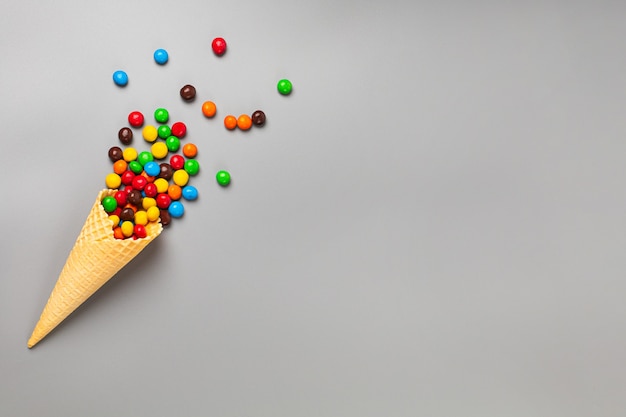 Ice cream cone with multicolored sweets on gray background