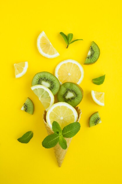 Ice cream cone with sliced lemon and kiwi on the yellow background. location vertical