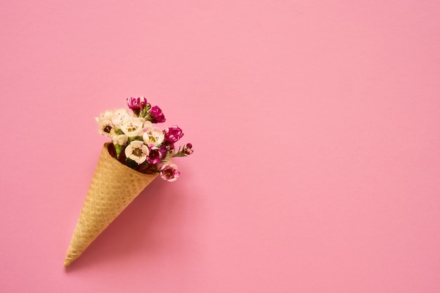 Ice cream cone with small flowers on pink background. Copy space, top view.