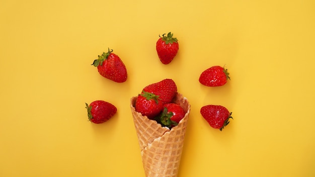 黄色の背景にイチゴとアイスクリームコーン。ワッフルコーンの赤いベリー。夏の写真