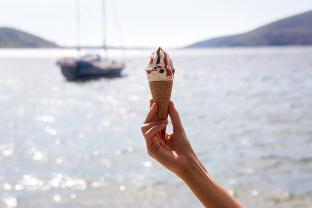 海とヨットの背景に女性の手でチョコレートとジャムとアイスクリームコーン