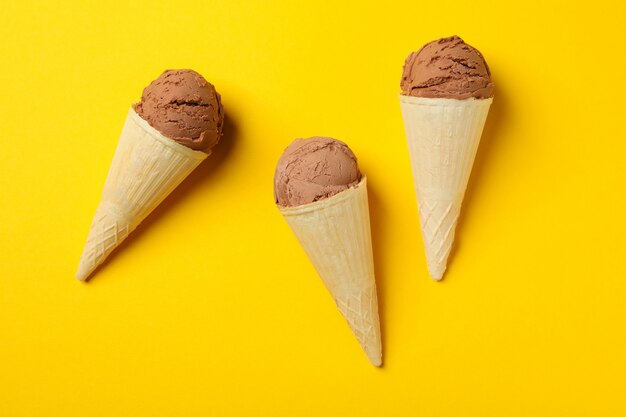 Ice cream in cones on yellow surface. Sweet food