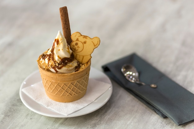 Десерт мороженого в вафельном стаканчике с шоколадным печеньем и креативным украшением на затуманенном светлом пространстве