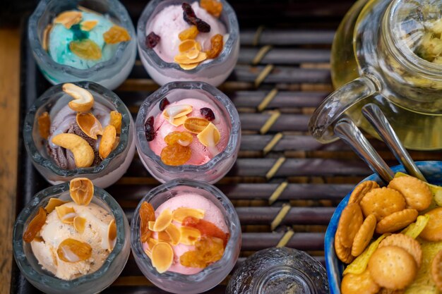 Ice cream in a glass bowl on a dark brown wooden tray With many toppings served on top