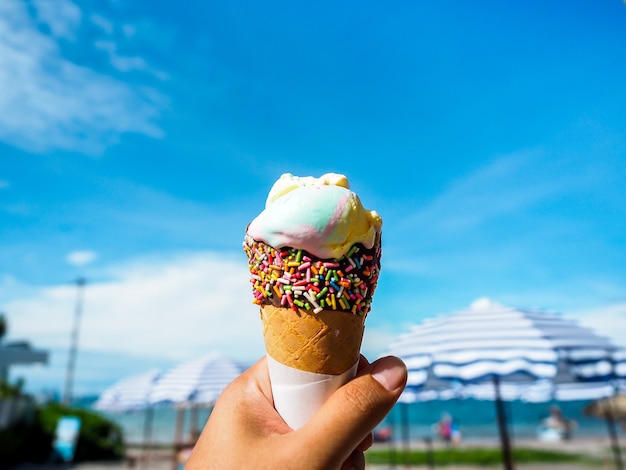 Ice cream in hand on beach and blue sky.