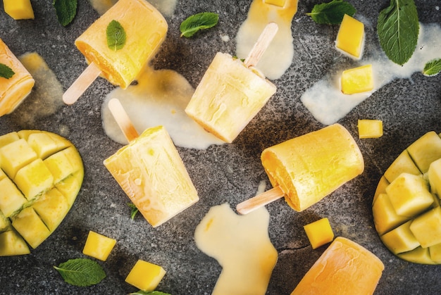 Ice cream, popsicles. Organic dietary foods, desserts. Frozen mango smoothie, with mint leaves and fresh mango fruit, on black stone table.   top view