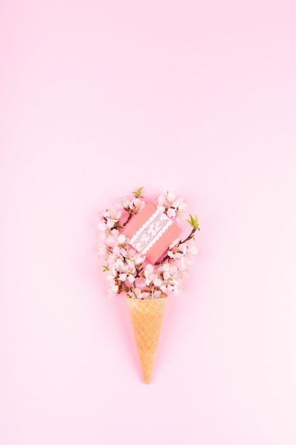 Ice cream waffle cone with colorful flowers and gift box on pink