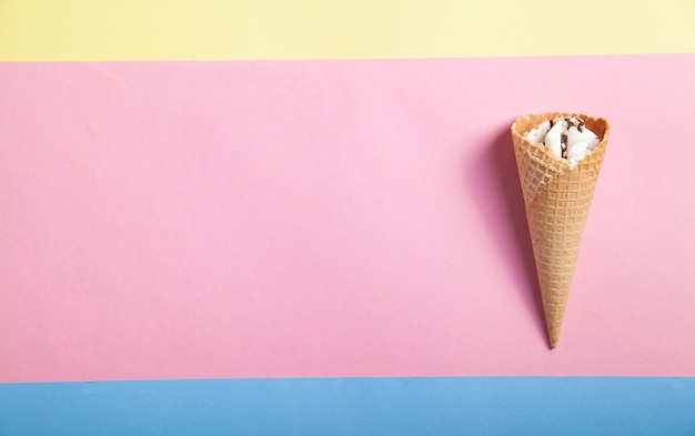 黄色、青、ピンクの背景にワッフル コーンのアイスクリーム。