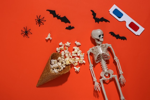 Ice cream waffle cones with popcorn, decorative bats and spiders, skeleton, 3d glasses on orange bright background. Top view. Scary movie. Flat lay halloween composition