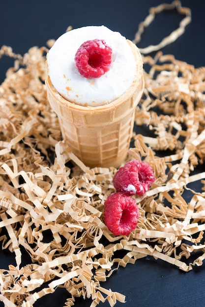 Ice cream with raspberry in waffle cone on wood