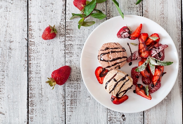 Ice cream with strawberries and chocolate on a white plate