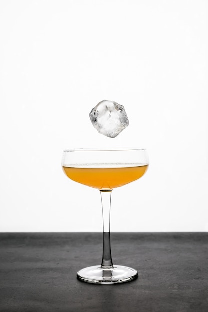 An ice cube falling into a coupe glass with an orange cocktail