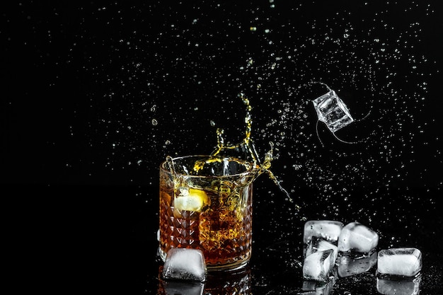 Ice cubes fall into a glass with whiskey Isolated shot of whiskey with splashes from falling ice fly in different directions freeze motion