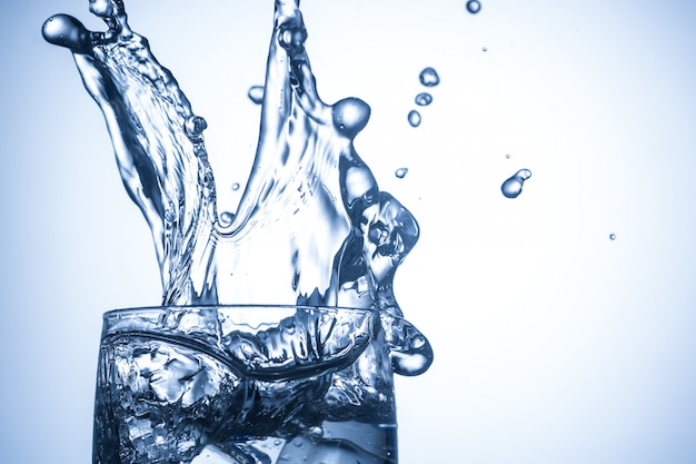 Ice cubes falling in glass with water splashes close up