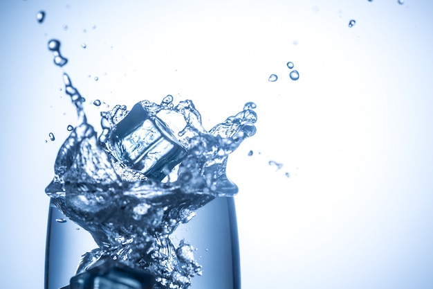 Photo ice cubes falling in glass with water splashes close up