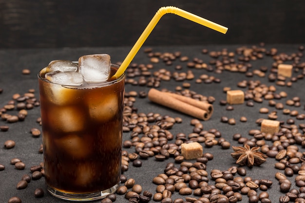 Ice cubes in glass with coffee close up. Coffee beans scattered on table.