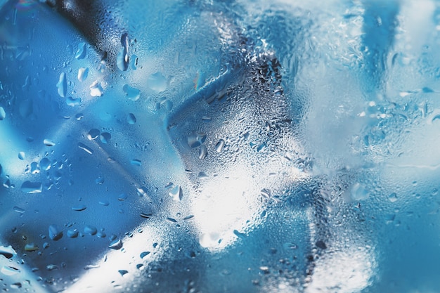 Фото Кубики льда в стакане с освежающей ледяной водой на синем фоне.