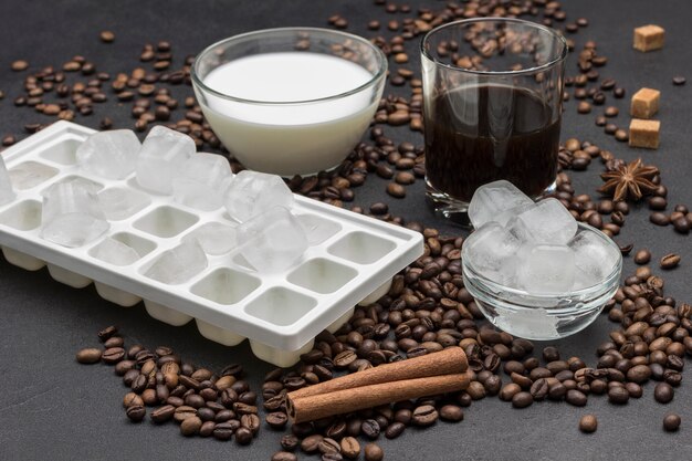 Фото Кубики льда в стеклянной миске, стакан молока и стакан кофе. кофейные зерна и палочки корицы