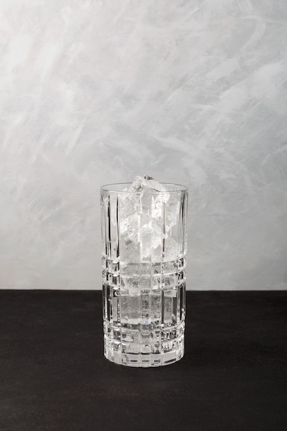 Ice cubes in tall cocktail glass. Grey background, copy space. Clear real ice for refreshing drinks.