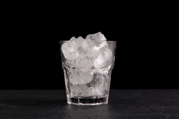 Ice cubes in a transparent glass. Dark stone countertop, black background, copy space.
