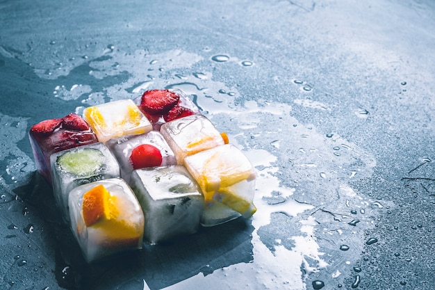 Ice cubes with fruit on a stone blue surface. The shape of the square. Mint, strawberry, cherry, lemon, orange. flat lay, top view