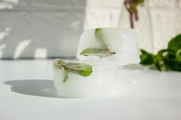Ice cubes with green mint leaves inside, on a white surface, place for text.