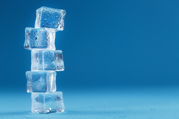 Ice cubes with water drops tower in a row on a blue background.