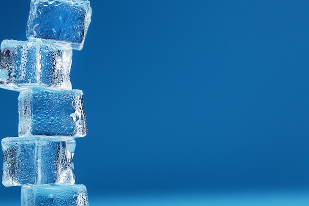 Ice cubes with water drops tower in a row on a blue background.