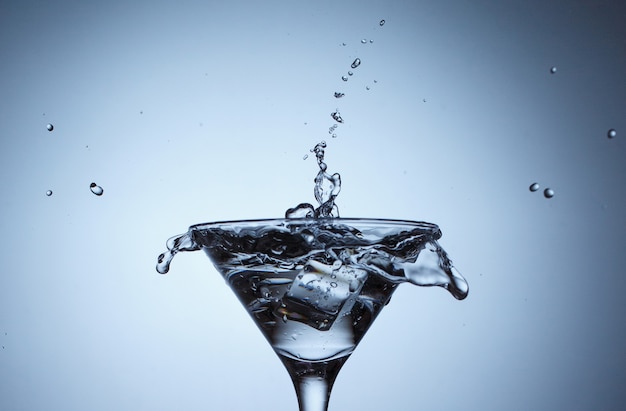 Ice in glass with water splash on blue surface