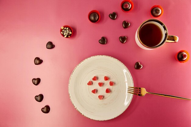 Ice hearts on white vintage plate with fork Chocolate hearts and decorated sweets Pink gradient background Creative romantic dinner Valentines Day concept View from above