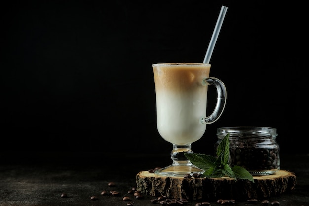 暗い背景のガラスビーカーにミルクと角氷を入れたアイスラテまたはアイスコーヒー。さわやかな飲み物。夏の飲み物。