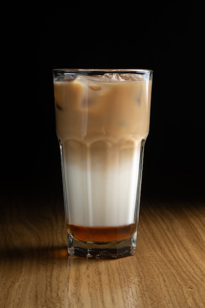 Ice latte macchiato coffee with syrup and ice in a transparent glass on a wooden table