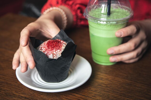 Primo piano di ghiaccio matcha latte e cupcake in un caffè in mani femminili