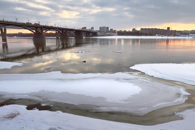 Photo ice on the ob river. oktyabrsky bridge, gorsky district in the distance in the evening