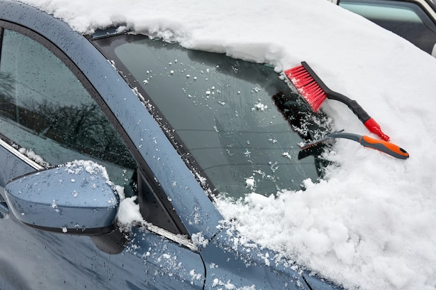 Ice scraper and brush for clearing automobile are on the hood of the car