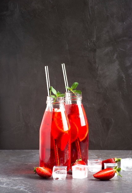 Ice strawberry lemonade with strawberries, lemon, mint and ice in glass bottles stands