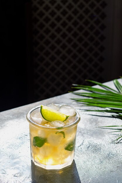 Photo ice tea with ice cubes lime mint leaves in the glass with palm leaves on gray stone background