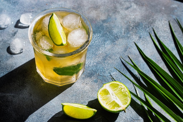 Ice tea with ice cubes lime mint leaves in the glass with palm leaves on gray stone background