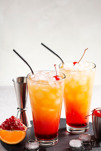 Ice tequila Sunrise-cocktails op een grijze betonnen tafel naast een jigger en cocktailkers