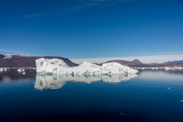 Photo iceberg in greenland fjord with reflection in calm water. sunny weather. golden hour.