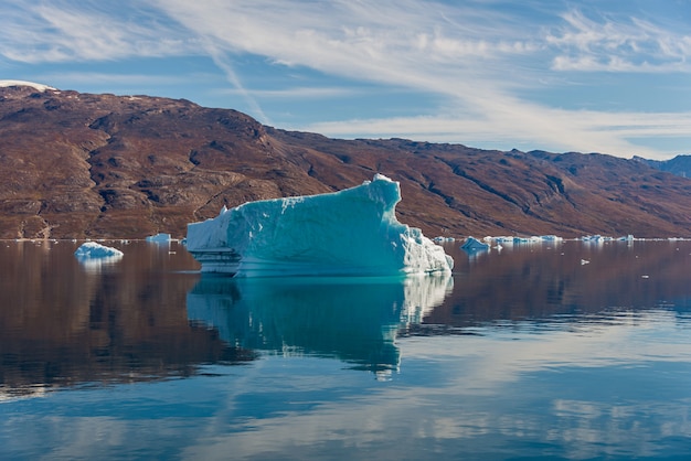 Iceberg in Greenland fjord with reflection in calm water. Sunny weather. Golden hour.