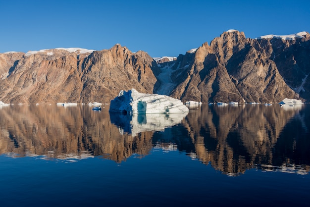 Iceberg in Greenland fjord with reflection in calm water. Sunny weather. Golden hour.