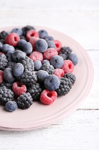 Iced berries on plate on color wooden background