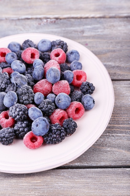 Iced berries on plate, on color wooden table