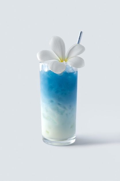 Iced blue butterfly pea latte drink with tropical flower decor. Healthy thai traditional cocktail in glass