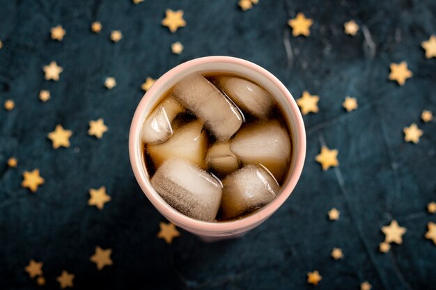 Iced coffee in a glass on a dark blue stone surface with stars.  Flat lay, top view