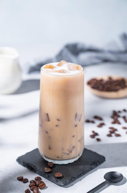 アイスコーヒーラテ (Iced Coffee Latte) はコーヒー豆と朝の影が付いた青い背景に牛乳をめた高層グラスで夏のリフレッシュコンセプトです