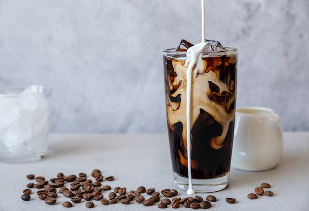 Iced coffee in tall glass with cream pouring from the top and coffee beans