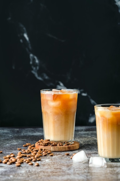 Iced coffee in a tall glass with poured cream, ice cubes and grains on an old rustic wooden table